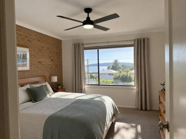 Black ceiling fan in a bedroom with brick feature wall and window view in Booker Bay