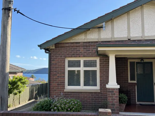 Overhead service cable and point-of-attachment bracket on a brick house with gable roof in Woy Woy