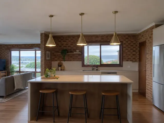 Three brass pendant lights above a kitchen island in a brick home interior in Ettalong Beach