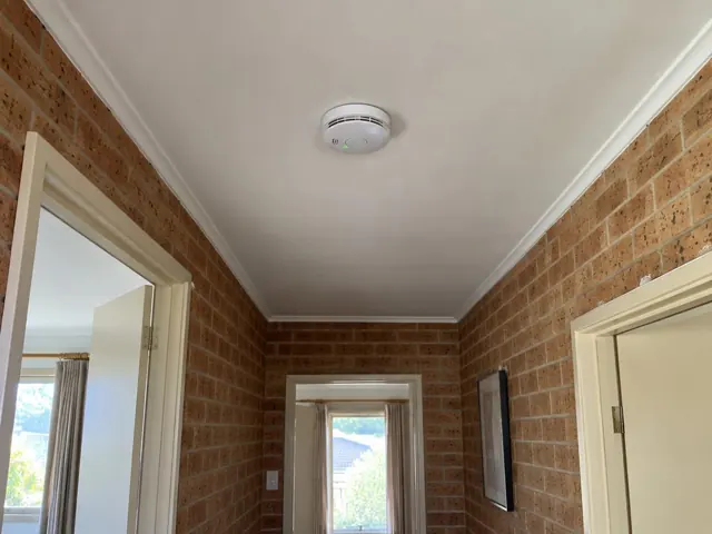 Smoke alarm mounted on a hallway ceiling in a brick-walled home in Booker Bay